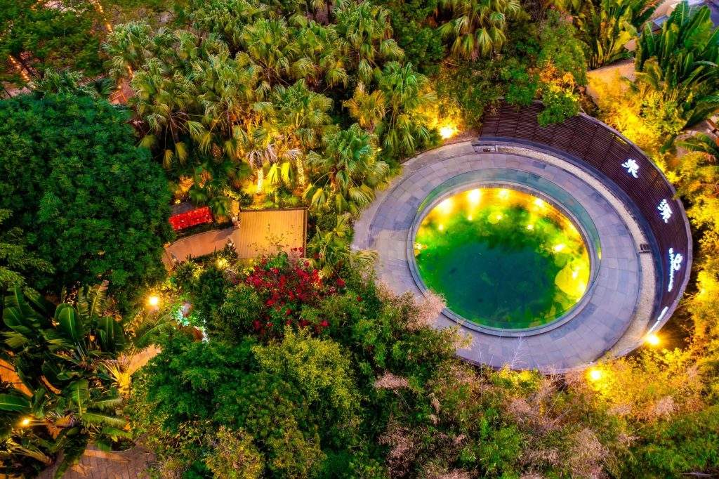 An aerial night time view of the source of the hot spring at Riyuegu Hotsprings where visitors can view the hot spring water bubbling to surface amidst dense tropical foliage and garden lights.