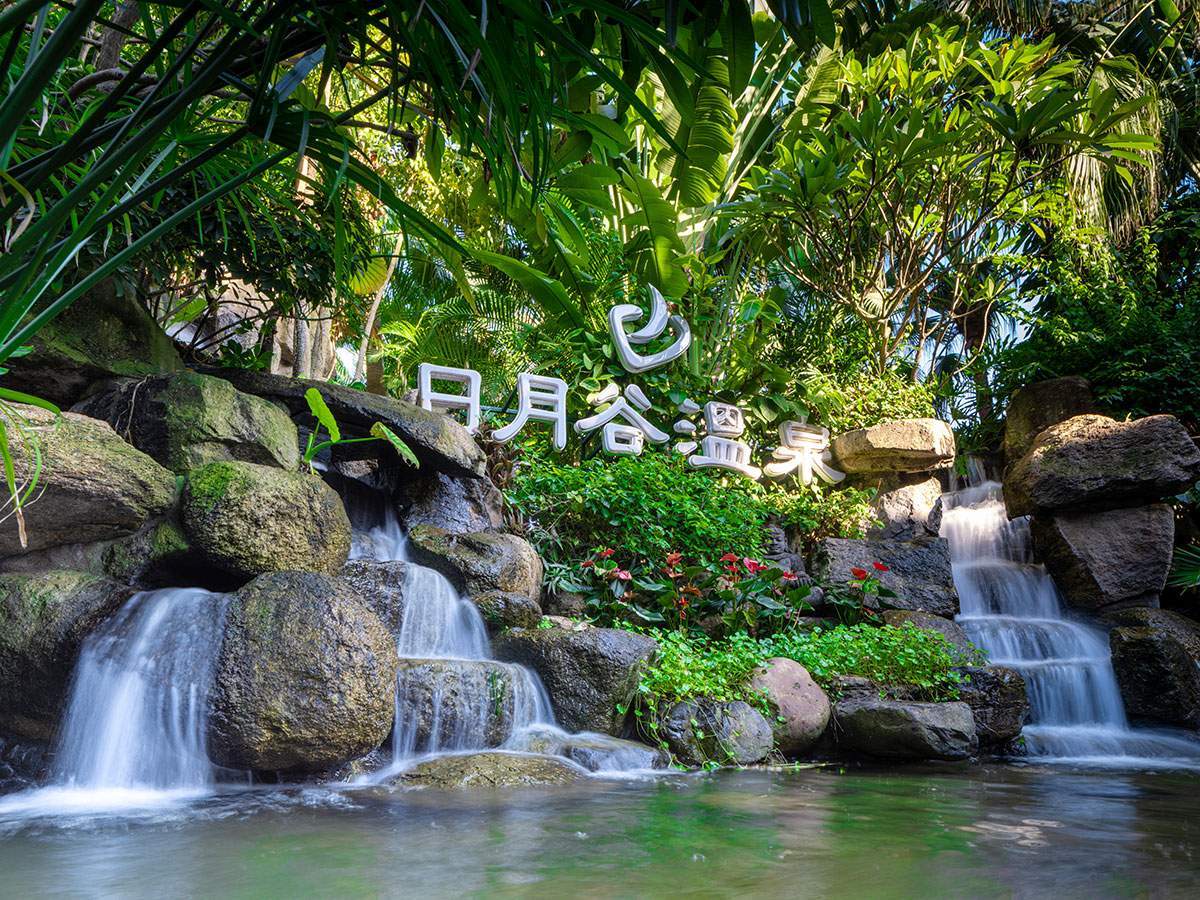 Riyuegu Hotsprings entrance signage set within landscaped greenery and waterfall features.